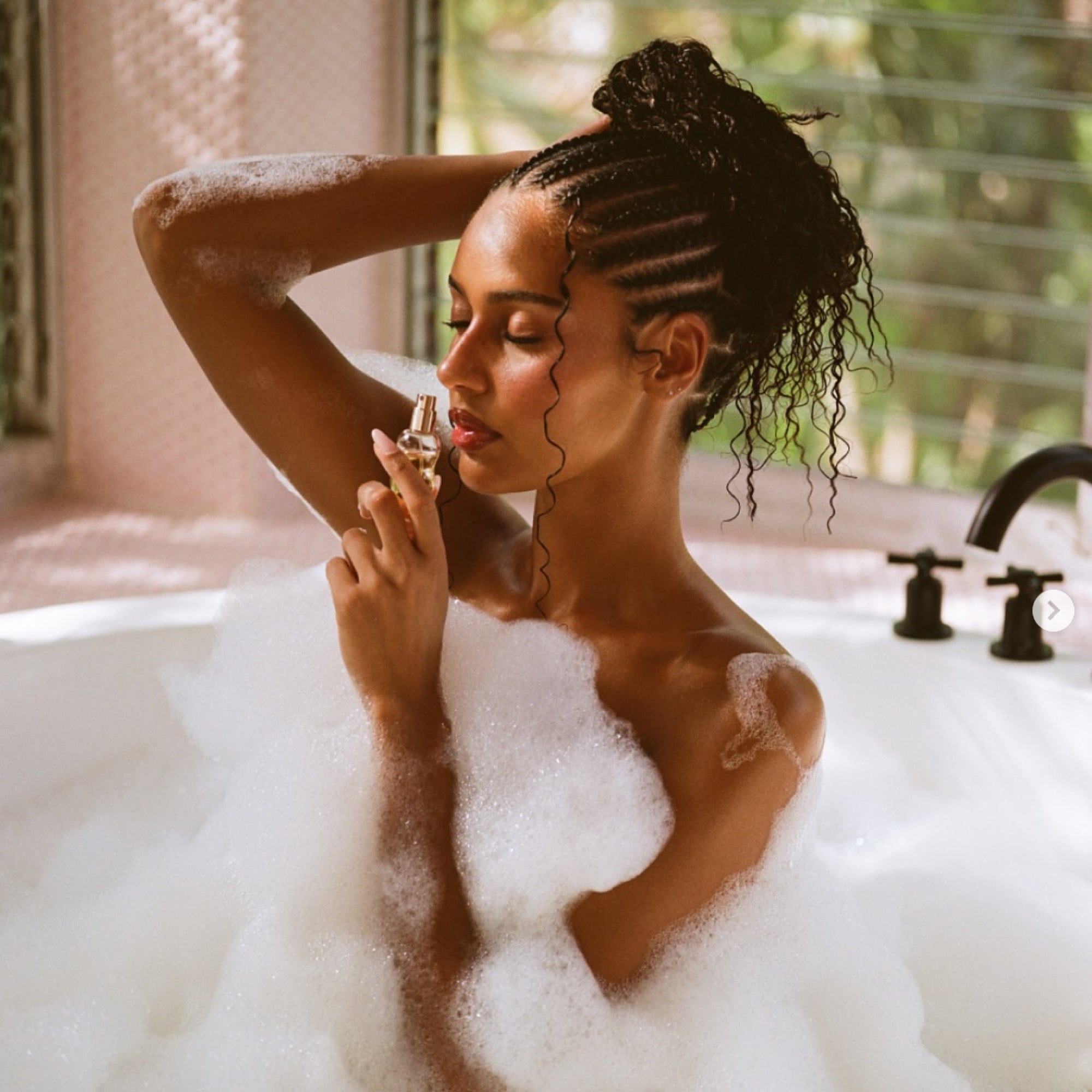 Model smelling the mini hair perfume in a bathtub.
