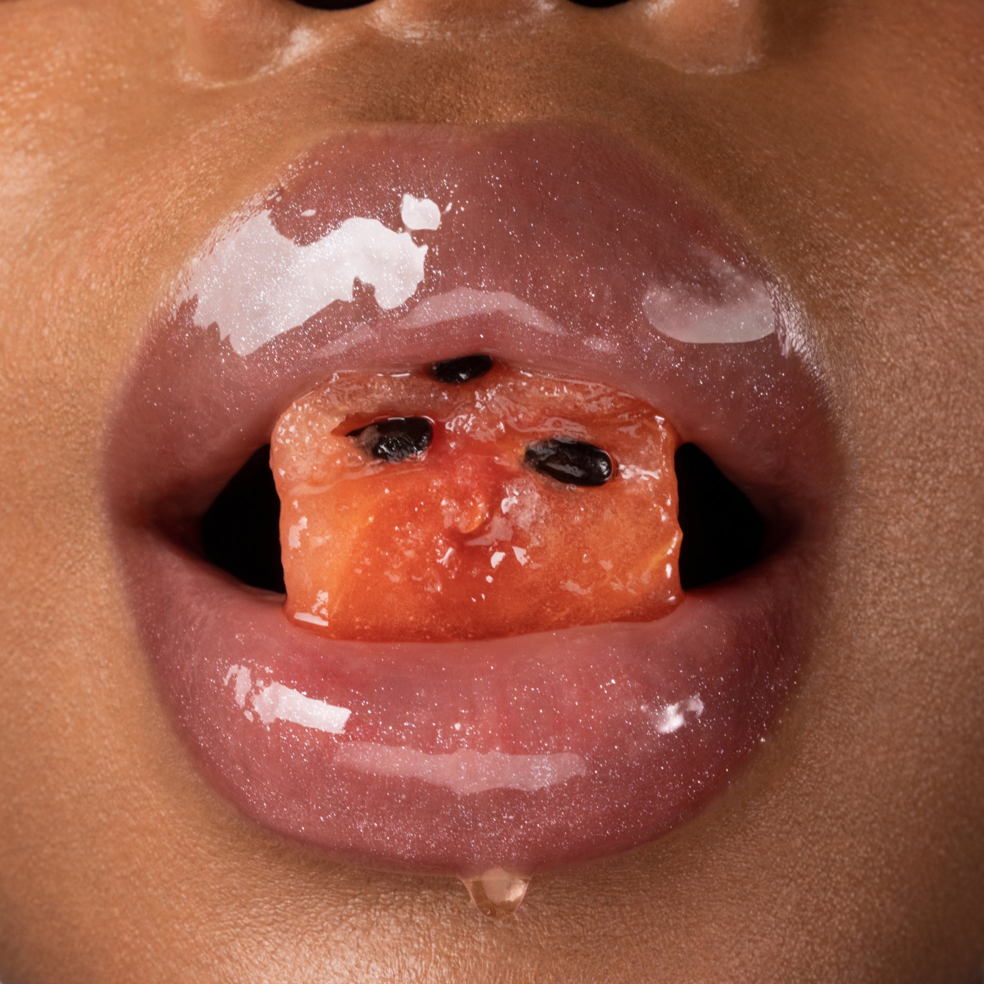 Glossy lips holding a piece of watermelon.