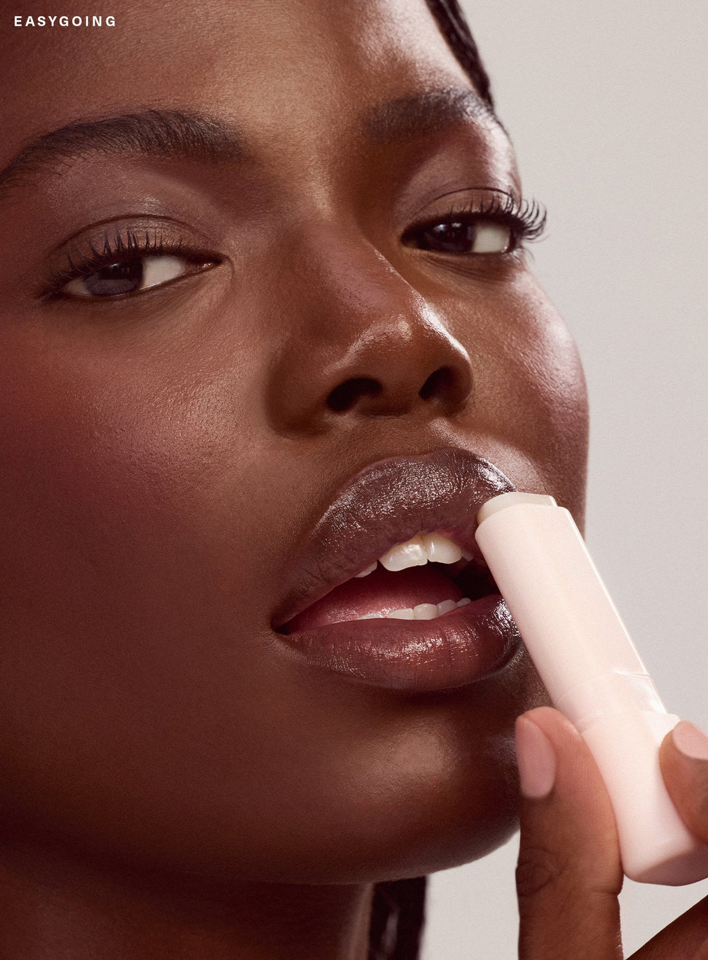 Easygoing| Model with deep brown skin applies Rare Beauty Find Comfort Lip Butter in the clear shade Easygoing