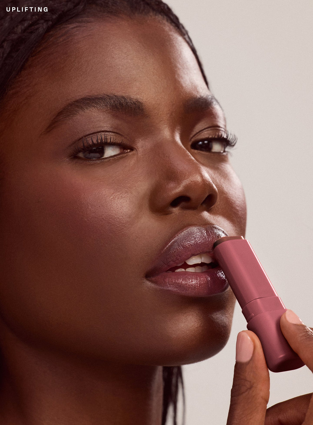 Uplifting| Close-up of model with deep brown skin applying Rare Beauty Find Comfort Lip Butter in shade Uplifting, a deep cool berry color
