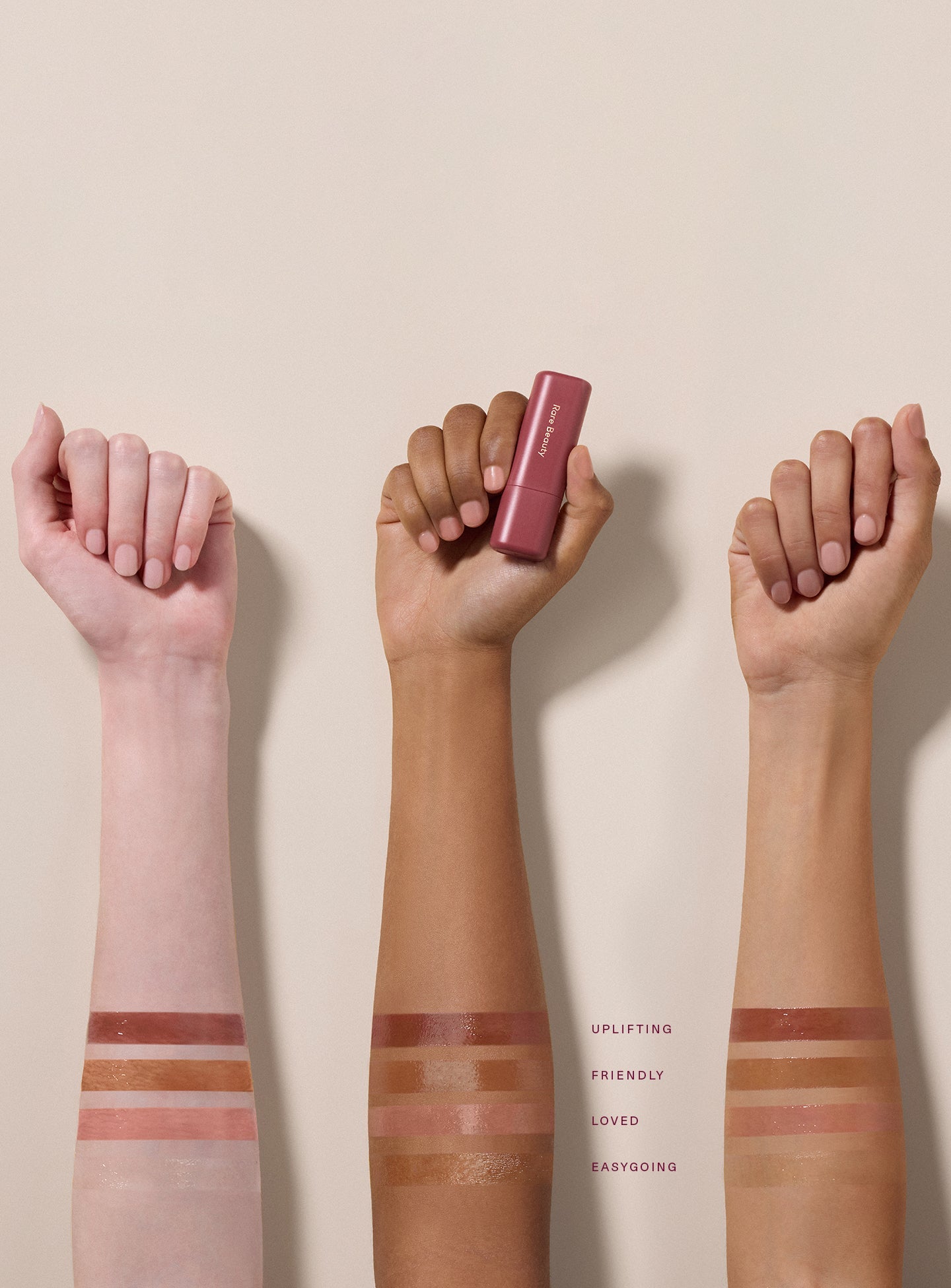 Three models with different skin tones show swatches of Rare Beauty Find Comfort Lip Butter shades on their arms