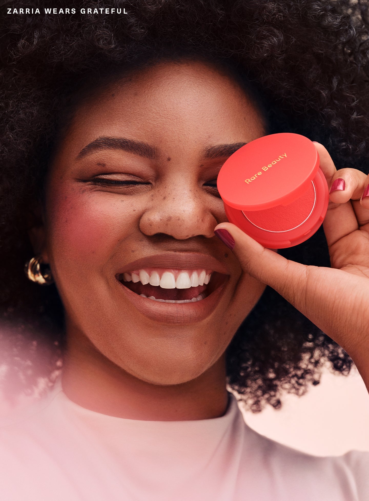 Grateful| Model Zarria applying Rare Beauty's Soft Pinch Matte Bouncy Blush in the soft red shade Grateful.