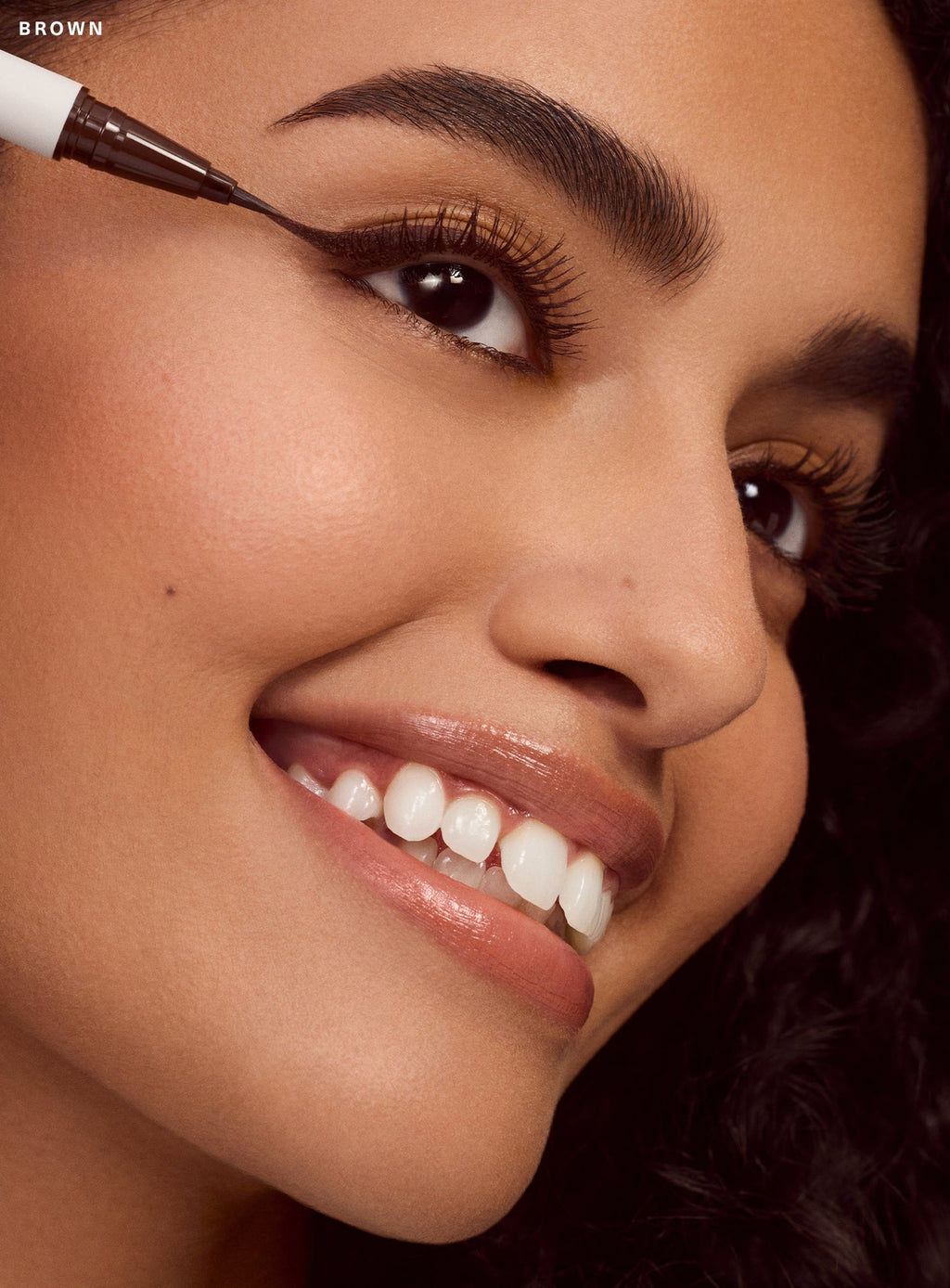 Model with light brown skin tone applying Rare Beauty's Perfect Strokes matte liquid liner in brown