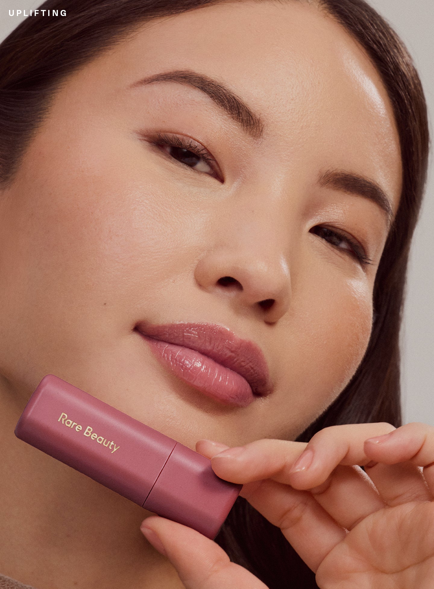 Uplifting| Close-up of a model with light skin wearing Rare Beauty Find Comfort Lip Butter in Uplifting, a deep cool berry shade