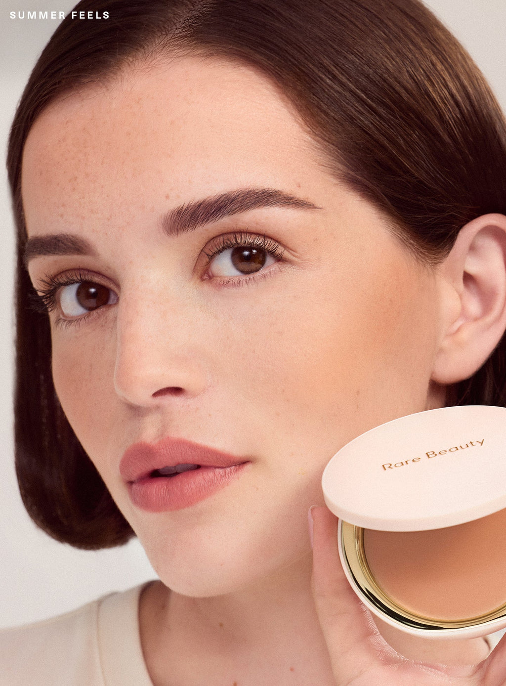 Summer Feels| Model with light-toned complexion models Rare Beauty Warm Wishes Soft Matte Powder Bronzer in Summer Feels a light tan shade with warm undertone