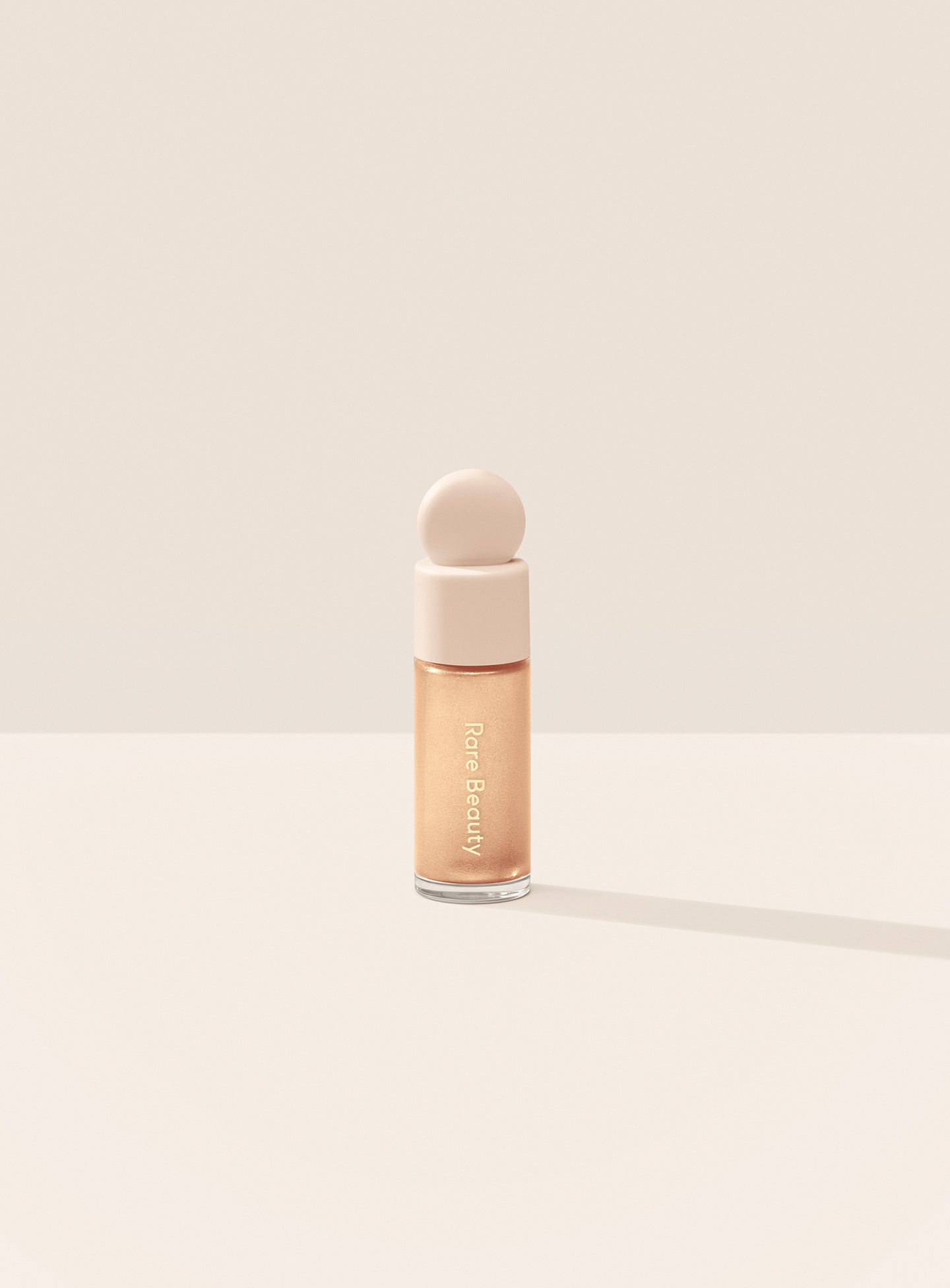 Exhilarate| Rare Beauty's Positive Light Liquid Luminizer Mini in the champagne shade Exhilarate against a neutral background.