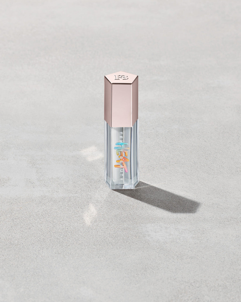 Closed tube of Gloss Bomb Heat lip gloss and plumper in the shade Glass Slipper on a grey background.