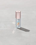 Closed tube of Gloss Bomb Heat lip gloss and plumper in the shade Glass Slipper on a grey background.