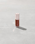 A close tube of Gloss Bomb Universal Lip Luminizer in the shade Hot Chocolit Fantasy on a grey background.