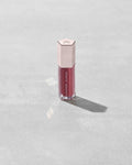 A closed tube of Gloss Bomb Universal Lip Luminizer in the shade RiRi on a grey background.