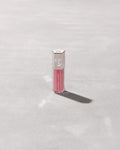 A closed tube of Gloss Bomb Universal Lip Luminizer in the shade Candy Soda on a grey background.