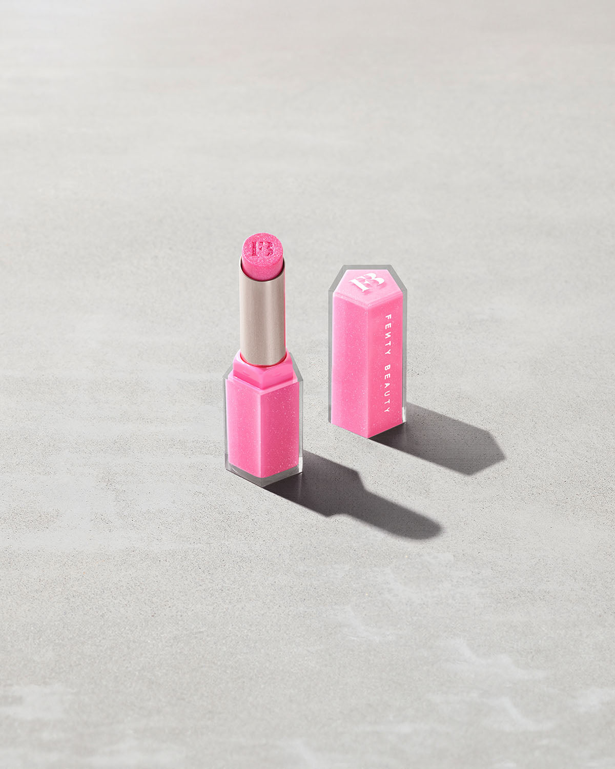 Open product shot of Gloss Bomb Stix Shimmer in shade Flamingo Fling on a concrete background.