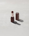 Open product shot of Gloss Bomb Stix Shimmer in shade Hot Chocolit on a concrete background.