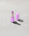 Open product shot of Gloss Bomb Stix Shimmer in shade Ice Amethyst on a concrete background.