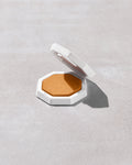 Open product shot of Demi'glow Light-Diffusing Highlighter in shade Rich Hunnie on a concrete backdrop.