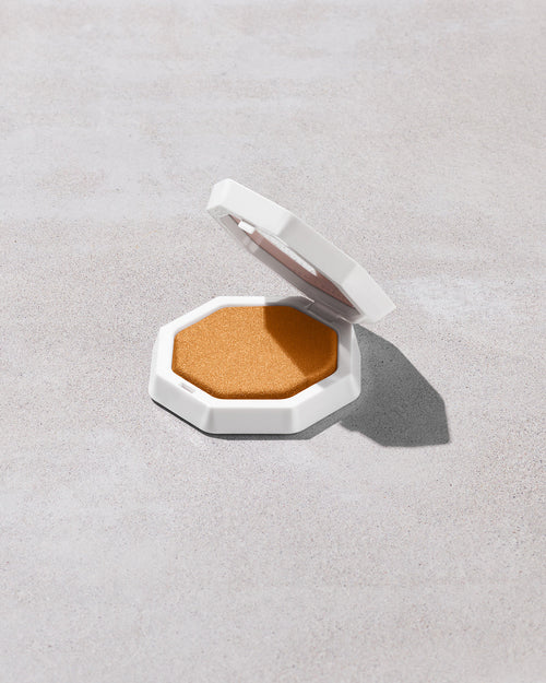 Open product shot of Demi'glow Light-Diffusing Highlighter in shade Rich Hunnie on a concrete backdrop.