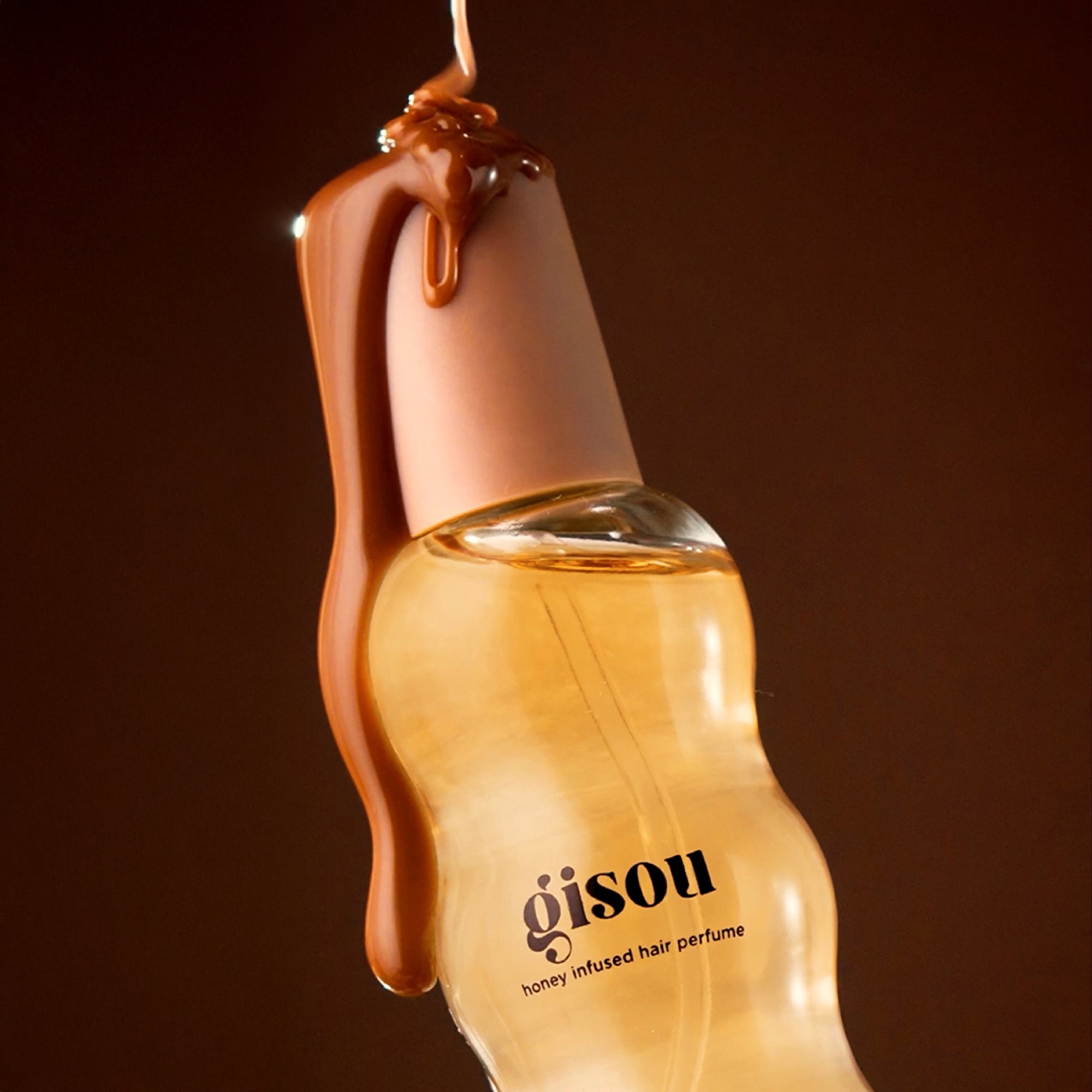 Close-up of Gisou Honey Infused Hair Perfume bottle with caramel dripping over the cap, highlighting the Sticky Toffee scent and glossy, honey-infused formula.