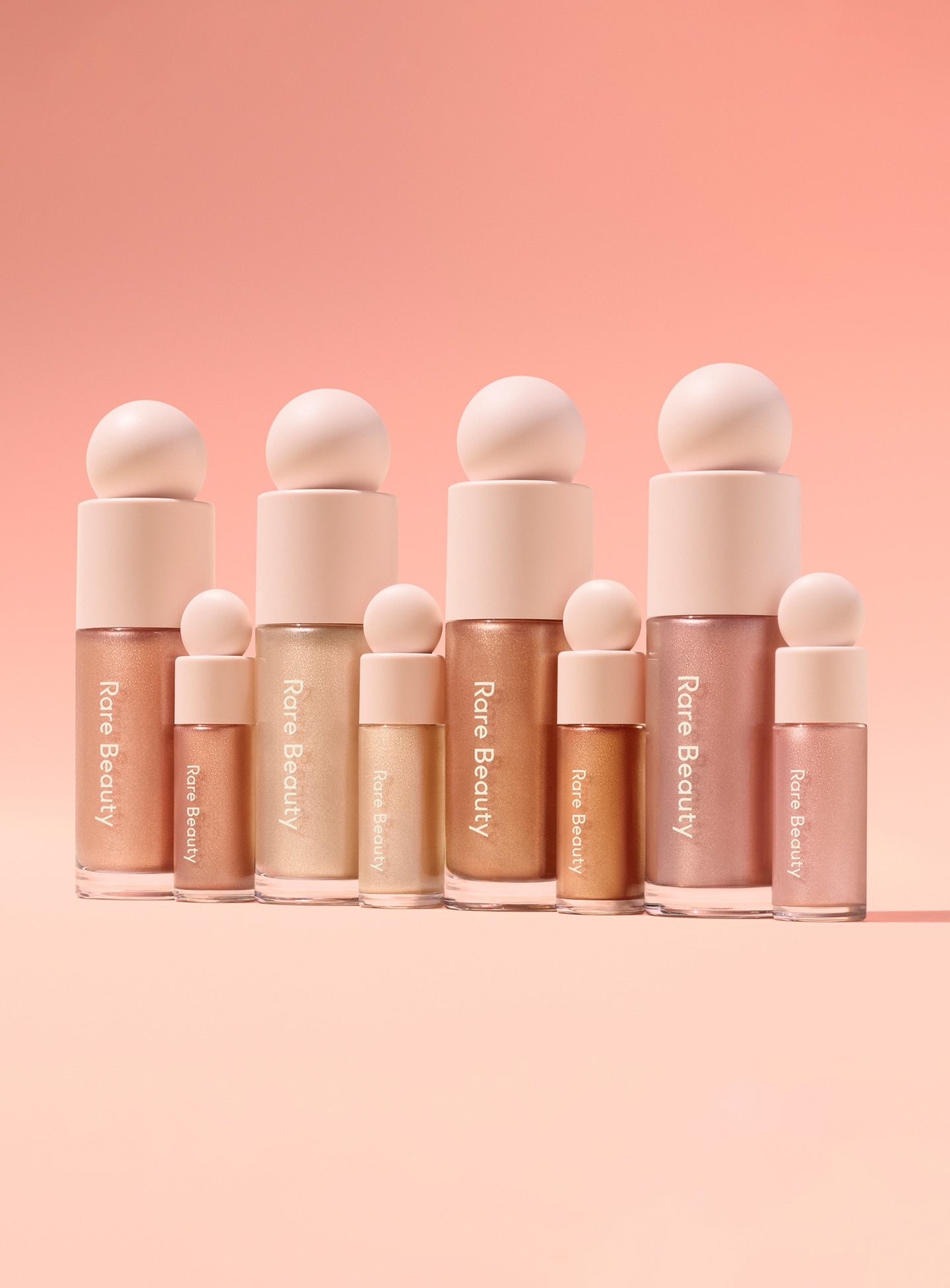 Every shade of Rare Beauty's Positive Light Liquid Luminizer in the regular and mini versions against a pink background.