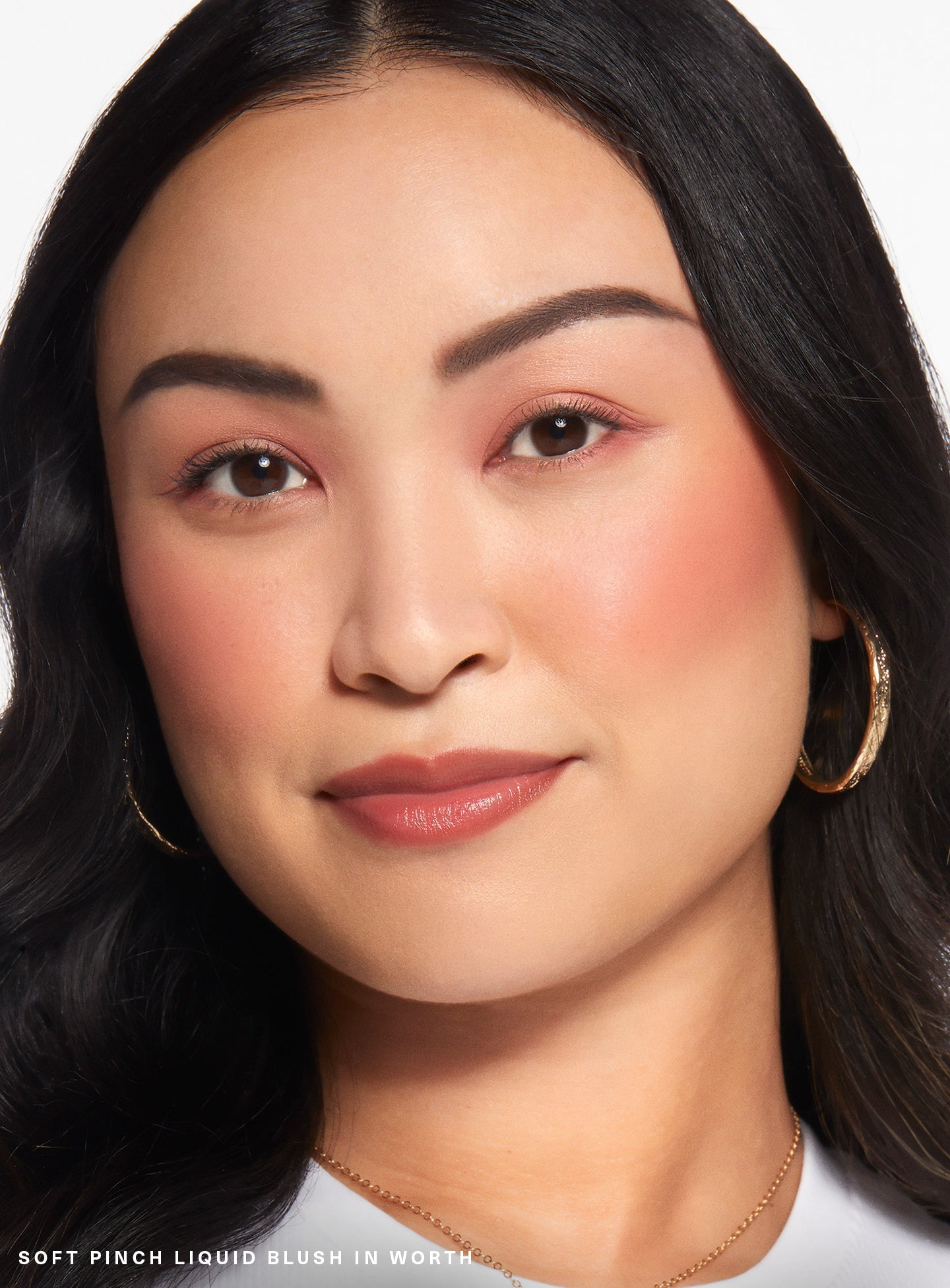 Worth| A model wearing Rare Beauty's Soft Pinch Liquid Blush in the dewy true rose shade "Worth."