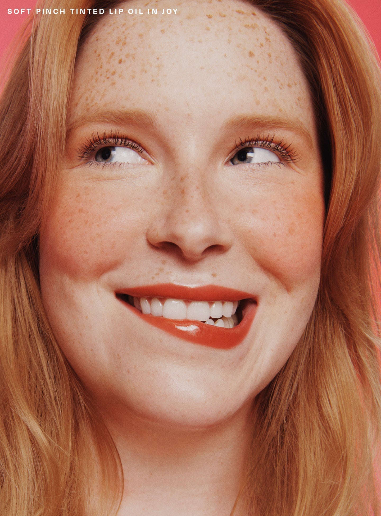 Joy| A model biting her lip and wearing Rare Beauty's Soft Pinch Tinted Lip Oil in shade "Joy".